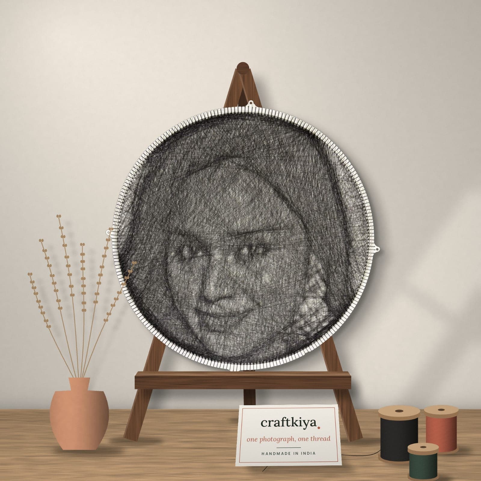 A hand-threaded 24-inch circular string-art portrait on a wooden easel beside a Craftkiya card and thread spools